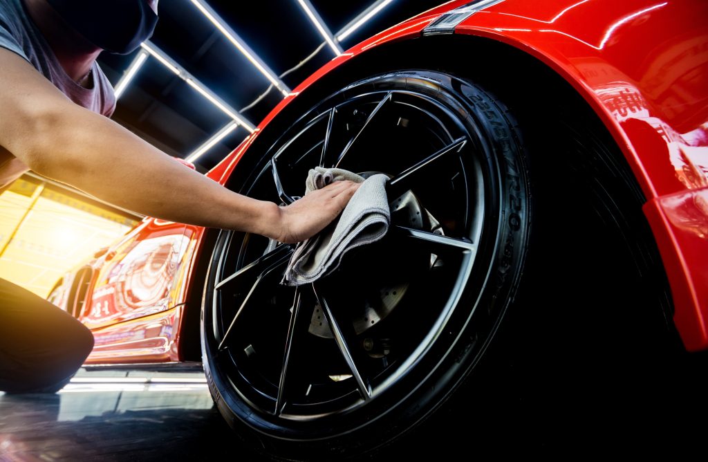 Car service worker polishing car wheels with microfiber cloth.
