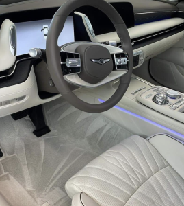 Luxurious car interior with a round steering wheel, digital dashboard, and light gray perforated leather seats.